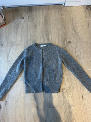 Grå stickad kofta från Zara strl S - Säljer en grå stickad kofta från Zara i storlek S. Koftan har rund hals, långa ärmar och knäpps med silvriga knappar framtill. Perfekt för lager-på-lager och chill dagar. Materialet är mjukt och värmande. Strl S