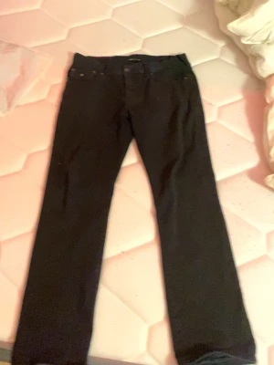 Svarta True Religion Ricky jeans - Svarta jeans från True Religion, modell Ricky Relaxed Straight. Klassisk femficksdesign med raka ben och avslappnad passform. Snygga metallknappar och detaljer, tillverkade i slitstarkt bomullsmaterial. Perfekt för dig som gillar streetwear och vill ha en clean look. Pris kan diskuteras 