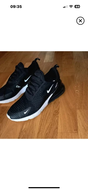 Nike Air Max 270 svarta sneakers - Svarta Nike Air Max 270 sneakers med vit sula och vita loggor. Ovandelen är i mesh med snygga detaljer och snörning. Skorna har en rund tå och synlig Air-enhet i hälen för extra komfort. Perfekta för dig som gillar sportig stil och streetwear. Använda i ca två månader fortfarande användbara enda nackdelen e tyget gått upp upp lite som man ser pö sista bilden men inget som syns de går o sy eller fixa  den som e händig men går använda oavsett för de ej trasiga eller nåt på så sättköptes för 1699