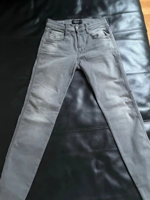 Replay Anbass grå slim jeans - Säljer ett par grå Replay Anbass jeans i slim fit med klassisk femficksdesign och snygga detaljer på bakfickorna. Jeansen har en smal passform och är tillverkade i mjukt jeansmaterial med lite stretch för extra komfort. Perfekt för dig som gillar stilrena och moderna jeans.