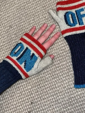 Stickade vantar med ON/OFF-mönster - Unika stickade vantar med texten ON och OFF i blått och svart. Vantarna har röda och vita ränder upptill och är mörkblå nedtill med blå kant. Perfekt för dig som gillar färgglada accessoarer med coolt mönster.