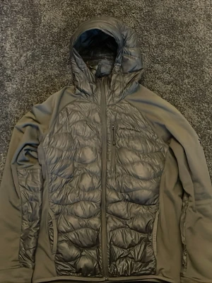 Svart pufferjacka med huva från Peak Performance - Säljer en svart pufferjacka från Peak Performance med snygg quiltad framsida och rygg. Jackan har huva, dragkedja hela vägen och praktiska fickor. Materialet är polyester och syntet, perfekt för kyliga dagar. Stilren design som funkar till många outfits.