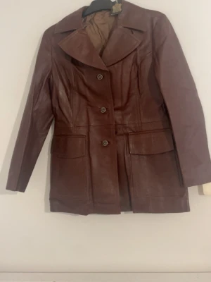 Brun skinnjacka äkta läder - Säljer en brun skinnjacka från MP i äkta läder. Jag köpte den för 149€ i Tyskland Jackan har stora slag, dekorativa knappar framtill och två stora fickor. Modellen är lite längre och har en klassisk, tidlös look. Är lite figursydd vid midjan. Perfekt för dig som gillar vintagevibbar och vill sticka ut med en snygg jacka. I storlek 40 alltså passar dig som har storlek M. Priset kan diskuteras!🩷