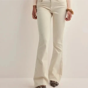 Bootcut jeans i ljus beige från Vero Moda - Snygga ljusbeige bootcut jeans från Vero Moda med klassisk femficksdesign och dragkedja. Byxorna har hög midja och är tillverkade i mjukt bomullsmaterial med lite stretch för skön passform. Perfekt för dig som gillar retrovibbar och stilrena färger.