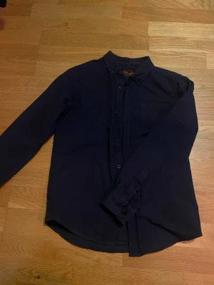 Mörkblå snygg skjorta från Skill - Snygg mörkblå skjorta från Skill med klassisk krage och bröstficka. Skjortan har långa ärmar och knäppning framtill. Tillverkad i mjuk bomull, perfekt för en chill och stilren look. I barn storlek 146-152