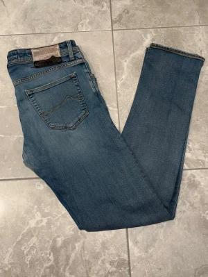 Jacob Cohën jeans - Snygga ljusblåa jeans från Jacob Cohën, har en svart läderpatch bak som har en del defekter på sig. Jeansen är perfekta för dig som gillar snygga och stiliga jeans! Jeansen är i storlek W33.