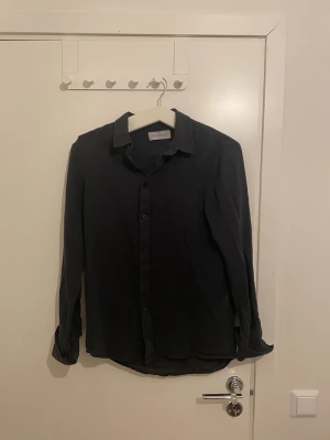 Svart skjorta från Pier One - Svart skjorta från Pier One med klassisk krage och knappar hela vägen framtill. Skjortan har långärmade ärmar och en rak, normal passform. Materialet känns mjukt och lätt, perfekt för dig som gillar stilrena och enkla plagg. Använd sparsam och inga defekter. Skick 7/10. Passar dig som är runt 175 cm. Hör av dig frågor eller funderingar!