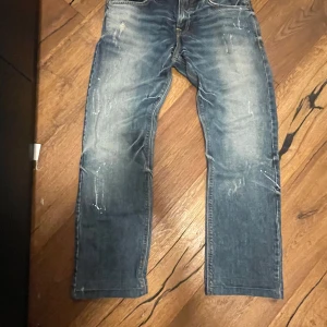 Archive jeans med bootcut från  LTB - Säljer ett par blå jeans från LTB med bootcut-snitt och coola slitningar samt ljusa tvättade detaljer. Jeansen har klassiska fem fickor och är tillverkade i jeansmaterial med en loose passform. Perfekt för dig som gillar en avslappnad stil.