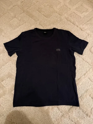 Marinblå från Hugo Boss - Snygg marinblå t-shirt från Hugo Boss med diskret logga på bröstet. Klassisk rund hals och korta ärmar, perfekt för en clean och stilren look. Mjuk bomull som känns skön mot huden. Passar dig som gillar enkla och tidlösa plagg.