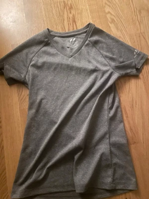 Grå t-shirt från Pro Touch - Säljer en grå t-shirt från Pro Touch i storlek XXS. T-shirten har v-ringad hals och är tillverkad i ett lätt och ventilerande syntetmaterial, perfekt för träning eller sport. Enkel och stilren design med korta ärmar och diskret logga på ärmen.