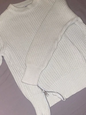 Vit stickad tröja från Gina Tricot - Säljer en vit stickad tröja från Gina Tricot i storlek S. Tröjan har grov ribbstickning, rund halsringning och en snygg silverfärgad dragkedja i sidan som detalj. Perfekt för kyliga dagar och enkel att styla till olika outfits.