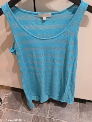 Turkos glittrig randig linnetopp - Säljer en turkos linnetopp i storlek 40/42 med glittriga ränder. Toppen är ärmlös och har en rundad halsringning. Perfekt för varma dagar och enkel att matcha med jeans eller shorts.