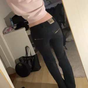 Svarta jeans med spetsdetaljer - Säljer ett par svarta Crocker jeans med snygga spetsdetaljer längs benen och guldfärgade dragkedjor på bakfickorna. Jeansen har låg midja och klassisk rak passform. Materialet är jeans med inslag av spets för en unik look.