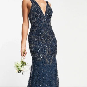 Asos maxi dress  - Hej! Jag är 170 cm lång och säljer en marinblå långklänning med djup v-ringning, och glittriga paljettdetaljer i ett elegant mönster. Har använt den en gång innan på min bal. Klänningen har figurnära passform och är täckt av skimrande pärlor och paljetter som ger en lyxig känsla. Perfekt för bal eller festkvällar!