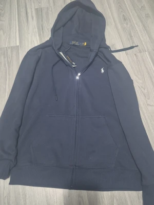 Blå polo ralph lauren zip up. Storlek S - En blå stilig ralph lauren zip up. Vet tyvvär ej om denna är äkta. Sonen fick den i somras och har aldrig använt den sen dess. Han har tydligen "Real checkat" denna och han sa att det såg bra ut. Men vi är ändå knte säkra. 