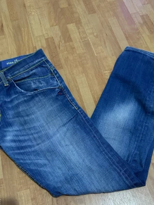 Blå jeansbyxor från Dondup - Snygga blå jeansbyxor från Dondup med klassisk femficksdesign och kontrastsömmar i gult. Byxorna har raka ben och detaljerade bakfickor med dragkedja. Materialet är slitstarkt jeans och färgen har en cool tvättad look med ljusare partier.