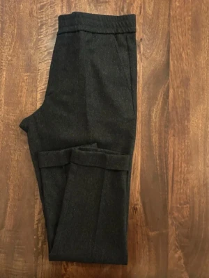 Mörkgrå kostymbyxor från Filippa K - Snygga mörkgrå kostymbyxor från Filippa K i klassisk rak modell. Byxorna har diskreta fickor och är tillverkade i ett mjukt ullmaterial som ger en stilren och clean look. Perfekta för dig som gillar minimalistisk och tidlös stil.