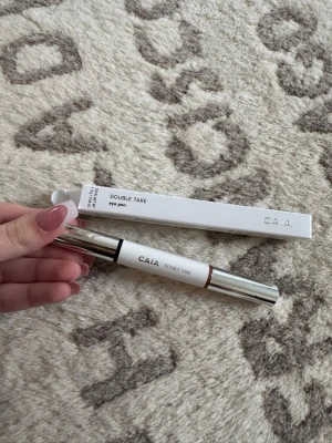 CAIA Double Take Eye Pen - Säljer en CAIA Double Take Eye Pen med två ändar, perfekt för att skapa olika ögonlooks. Pennan har en vit och silver design med texten 'TO PM' på förpackningen. Ena sidan är brun, vilket passar för mjuka och naturliga linjer. Kommer i originalförpackning.