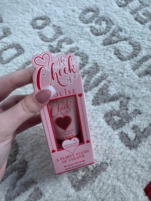 The Cheek of It Liquid Blush Tender Touch - Flytande rouge från Louise i nyansen Tender Touch. Kommer i en söt rosa förpackning med hjärtdetaljer och fönster som visar produkten. Ger en fräsch och flirtig färg till kinderna. Perfekt för dig som vill ha en naturlig och mjuk look.