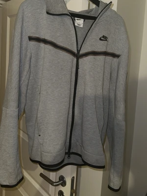 Grå nike tech  - Grå Nike tech hoodie med dragkedja, mycket bra skick, knappt använd . Mjuk och skön med klassisk Nike tech-design. Inga defekter. Perfekt för både träning och vardagsbruk.