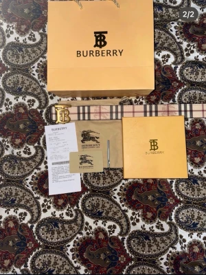 Burberry bälte med klassiskt rutmönster - Säljer ett Burberry bälte med det ikoniska beigea, röda och svarta rutmönstret och en stor guldfärgad BB-logga som spänne. Bältet är i canvas med detaljer i skinn och kommer med originalpåse o box. 110 CM Använt 1 gång