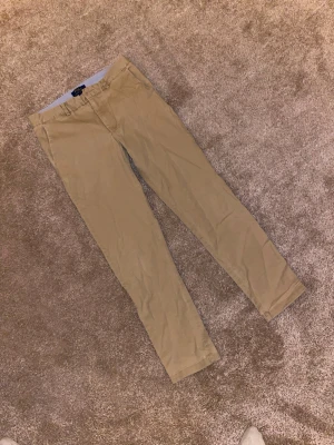 Beige chinos från Polo Ralph Lauren - Snygga beige chinos från Polo Ralph Lauren i klassisk rak modell. Byxorna har bälteshällor och stängs med dragkedja och knapp. Tillverkade i mjuk bomull som är skön att ha på sig. Perfekta för en chill och stilren look. Knappen är sönder!