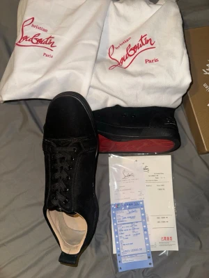 Svarta sneakers från Christian Louboutin - Säljer ett par svarta sneakers från Christian Louboutin med klassisk röd sula och snygg signatur. Skorna har snörning, rund tå och är tillverkade i mocka med skinnfoder. Perfekt för dig som vill ha något lyxigt och stilrent med en unik touch.