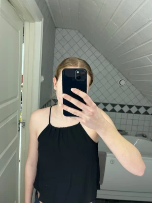 Svart linnetopp från H&M Divided - Svart linnetopp från H&M Divided med tunna axelband och rak halsringning. Toppen är ärmlös och har en luftig passform, perfekt för varma dagar. Tillverkad i ett lätt och mjukt polyestertyg som känns skönt mot huden.