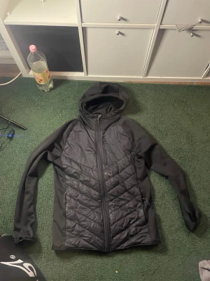 Svart fin jacka fint skick - Svart pufferjacka från Meraklon med quiltad framsida och huva. Jackan har dragkedja hela vägen, två sidofickor med dragkedja och en sportig look. Materialet är polyester och syntet, perfekt för kyliga dagar. Snygg och funktionell design för dig som gillar streetstyle. 1hål i båda fickorna men det gör inget 