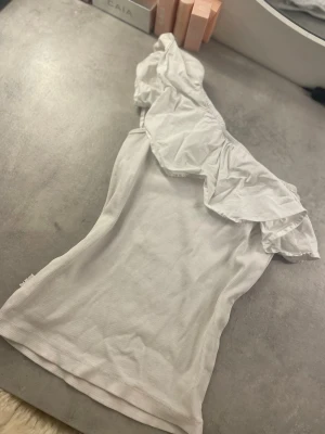 Vit topp med volang från Molo - Säljer en vit topp från Molo i storlek 158/164. Toppen har en bred volang längs halsringningen och är offshoulder med ribbad struktur i tyget. Materialet är mjukt och stretchigt, perfekt för dig som gillar en feminin och trendig look.🤍