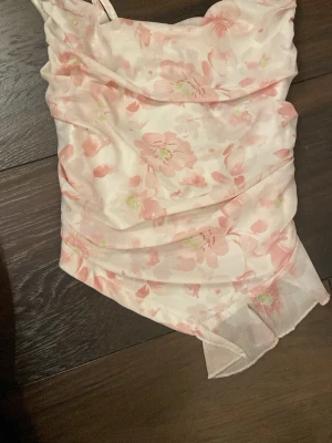 Blommig ljusrosa linnetopp - Söt linnetopp med tunna axelband och blommigt mönster i ljusrosa och vitt från shein. Toppen har en lätt rynkad effekt framtill och är gjord i ett tunt, luftigt material som känns perfekt för varma dagar.