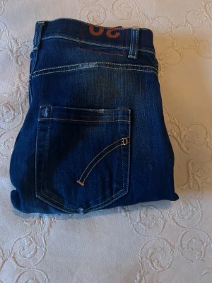 Blå Dondup mius jeans  - Säljer ett par snygga Dondup mius jeans i mörkblå tvätt med klassiska fem fickor och kontrastsömmar. Jeansen har en slim passform och raka ben, med Dondup loggan på bakfickan. Perfekt för dig som gillar stilrena och moderna jeans.