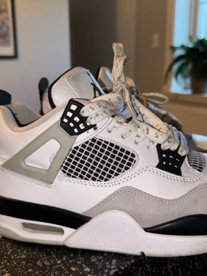 Nike Air Jordan 4 White/Black/Grey - Säljer ett par Nike Air Jordan 4 i vitt, svart och grått. Skorna har klassisk meshpanel på sidan, detaljer i mocka och skinn samt ikoniska Jumpman-loggan på hälen. De har snörning och en chunky sula med svart och vit färg. Perfekta för dig som gillar streetwear och sneakers med retrovibe.
