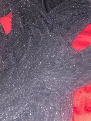 Svart glittrig omlottklänning Sister M - Perfekt för nyår!  Supersnygg svart omlottklänning från Sister i storlek M. Klänningen har långa ärmar, v-ringad hals och är täckt av glittriga detaljer som ger en festlig vibe. Knytband i midjan för extra passform och stil. Perfekt för dig som vill sticka ut med lite glitter.