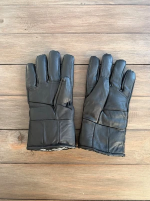 Svart skinnväst med quiltad design - Säljer en svart väst i skinn med quiltad look och raka linjer. Västen har en klassisk form och är fodrad för extra värme. Perfekt för dig som gillar stilrena och tidlösa plagg med lite edge. Passar till många olika outfits och ger en cool vibe.