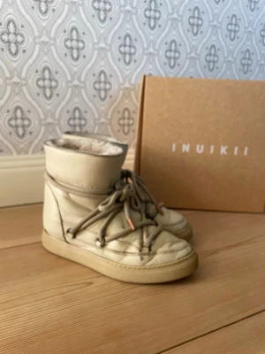 Beige Inuikii boots med snörning - Säljer ett par beige skor från Inuikii. Skorna har en platt sula och är fodrade med mjukt pälsmaterial på insidan för extra värme. Utsidan är i skinn och nya orginal sulor medföljer. Nypris 3700 kr.