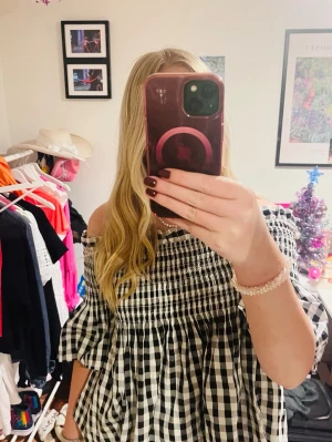 Svartvit rutig offshoulder blus - Säljer en söt blus med svartvitt rutigt mönster och offshoulder-design. Blusen har volangiga, korta ärmar och smock upptill som ger en snygg passform. Materialet känns lätt och luftigt.  Passar dig som gillar trendiga och bekväma toppar. storlek M men passar även S 