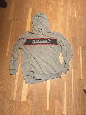 Grå hoodie - Grå hoodie ifrån Jacknjones. Schysst tryckning och stilren tröja. Funkar till det mesta och otroligt skön. Kom dm vid frågor