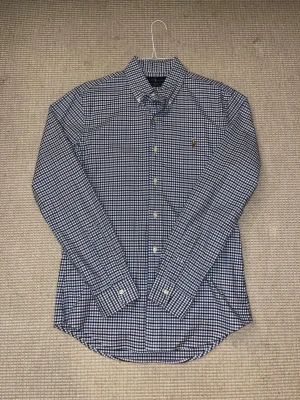 Blårutig skjorta från Ralph Lauren - Snygg blårutig skjorta från Ralph Lauren i stretchig bomull. Klassisk button-down krage, vita knappar och broderad logga på bröstet. Slim fit-modell som sitter schysst och har lång ärm. Perfekt för dig som gillar stilrena och tidlösa plagg. Köp ej via insta box helst PostNord.