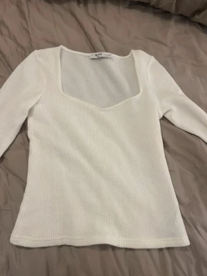 Vit ribbad långärmad topp från NA-KD - Säljer en vit långärmad topp från NA-KD i storlek S. Toppen har en fyrkantig, djup urringning och är ribbad i materialet vilket ger en snygg struktur. Passformen är normal och materialet känns mjukt och stretchigt, perfekt till jeans eller kjol.