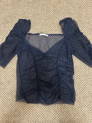 Blå prickig meshblus från Zara - Trendig blå meshblus från Zara med vita prickar och v-ringning. Blusen har puffiga korta ärmar och är lätt transparent, perfekt för en cool och stilren look.