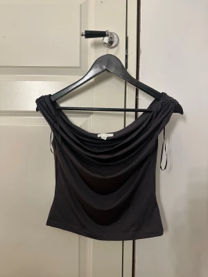Svart off shoulder topp H&M - Trendig grå off shoulder topp från H&M med draperad urringning och korta ärmar. Nyskick och aldrig använd då jag inte gillade den på mig. Köpt i somras. 