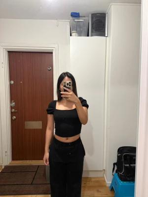 Svart croppad ribbad topp - Säljer en svart croppad topp med puffiga korta ärmar och fyrkantig halsringning. 