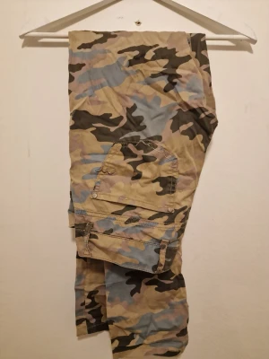 Cargopants i camouflage-mönster - Cargopants med klassiskt camouflage-mönster i beige, grön, blå och brun. Perfekta för dig som gillar streetwear och vill sticka ut lite extra.