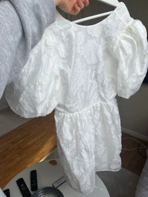 Vit studentklänning med puffärm Gina Tricot - Supersöt vit kortklänning från Gina Tricot, förra årets student kollektion, med puffärmar och blommigt strukturmönster. Perfekt till studenten eller midsommar! Helt oanvänd