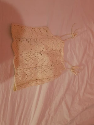 Stickad ljusbeige linnetopp - Supersöt stickad linnetopp i ljusbeige med knytbara axelband. Toppen har ett vågigt hålmönster och är perfekt för varma dagar. Passar dig som gillar en feminin och trendig stil.