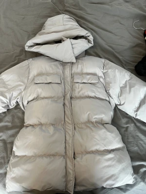 Beige pufferjacka med huva - Snygg beige pufferjacka med stor huva och två bröstfickor. Jackan har quiltad design, dragkedja framtill och en oversized passform som ger en chill vibe. Perfekt för kalla dagar när du vill vara både varm och stilren.