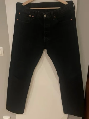 Svarta Levi's 501 jeans straight fit - Klassiska svarta Levi's 501 jeans med rak passform och knappgylf. Jeansen har fem fickor, ikonisk röd Levi's-tag på bakfickan och är tillverkade i slitstark bomullsdenim. Perfekta för en clean och tidlös look. Hör av er vid minsta fråga 🤗🤗