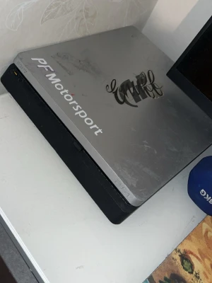 PlayStation 4 silver med dekaler - Säljer en PlayStation 4 konsol i silver med PF Motorsport och grafitti-dekaler på ovansidan. Konsolen har en stilren, rektangulär form och är tillverkad i plast och metall. Perfekt för gaming och filmkvällar. Funkar felfritt har inte använt så extrem mycke på senaste därför ja säljer de laddare och alla sladdar följer med det är lite repigt men inget som skadar innehållet 
