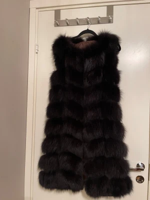 Svart lång pälsväst ÄKTA - ✨Snygg svart lång pälsväst. Västen har en lyxig känsla och är perfekt för att ge din outfit en extra edge. Passar dig som vill sticka ut och hålla dig varm under kalla dagar✨